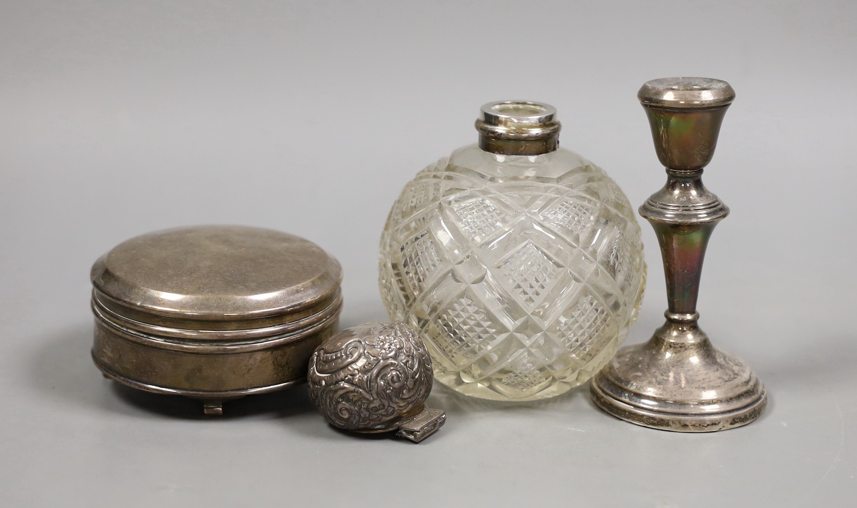 An Edwardian repousse silver mounted cut glass scent bottle(a.f.), a silver trinket box (no interior) and a silver mounted dwarf candlestick.